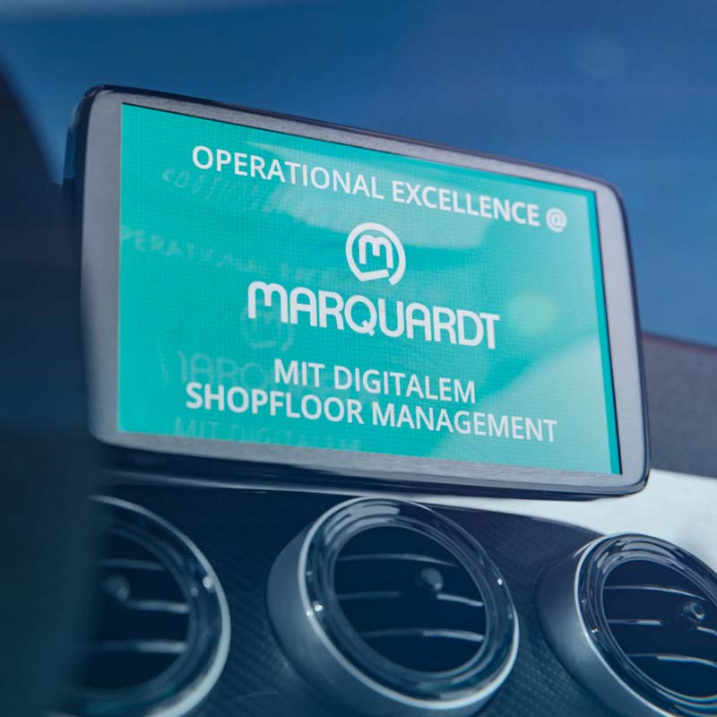 Head-up Display in Auto zeigt Webinar-Titel: Marquardt Operational Excellence mit digitalem Shopfloor Management